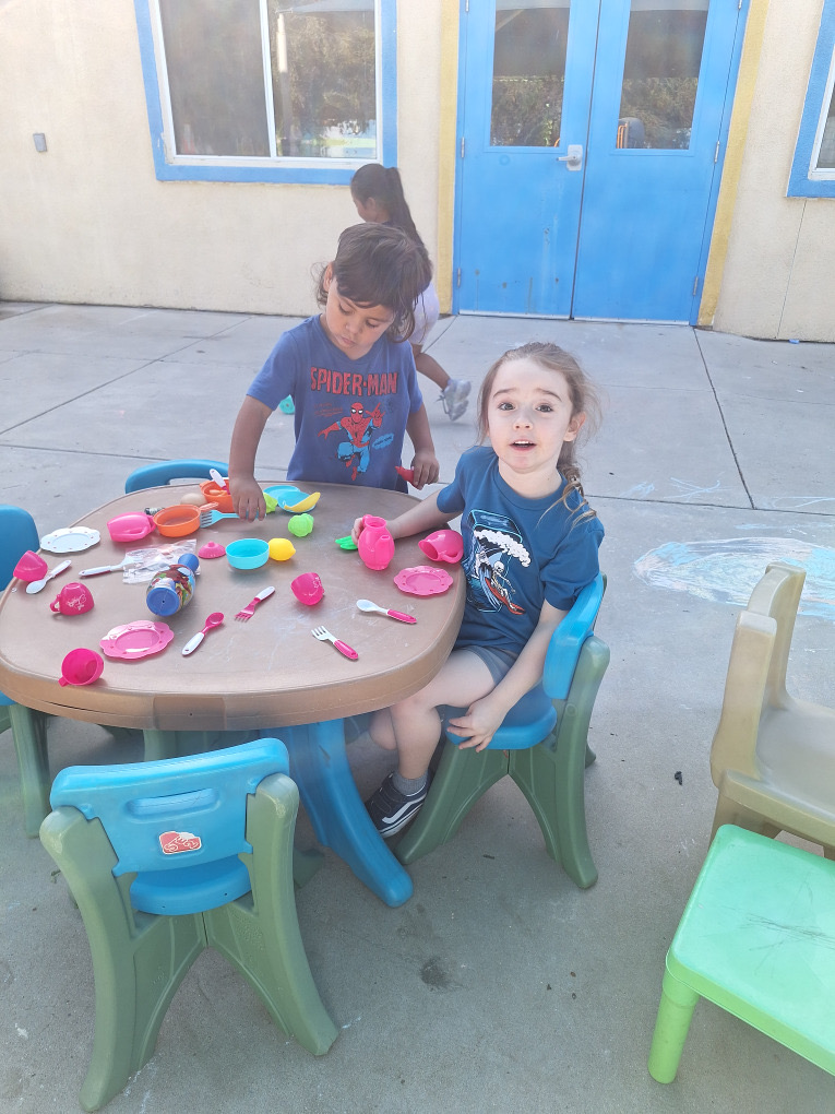 Children playing with pretend dishes at an outdoor table